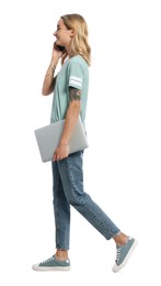 Young woman with laptop talking on smartphone and walking against white background