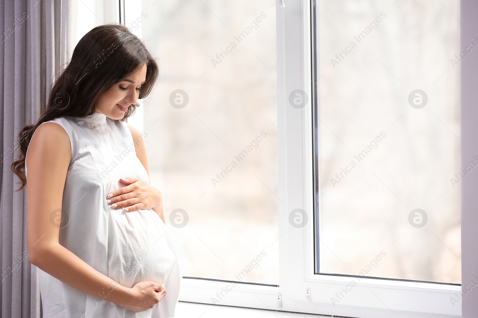 Photo of Beautiful pregnant woman near window at home