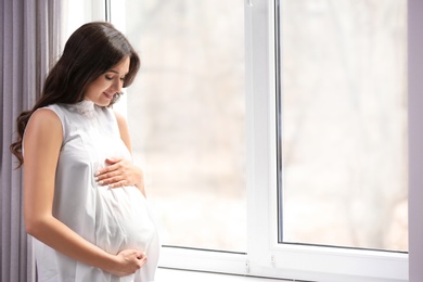 Photo of Beautiful pregnant woman near window at home