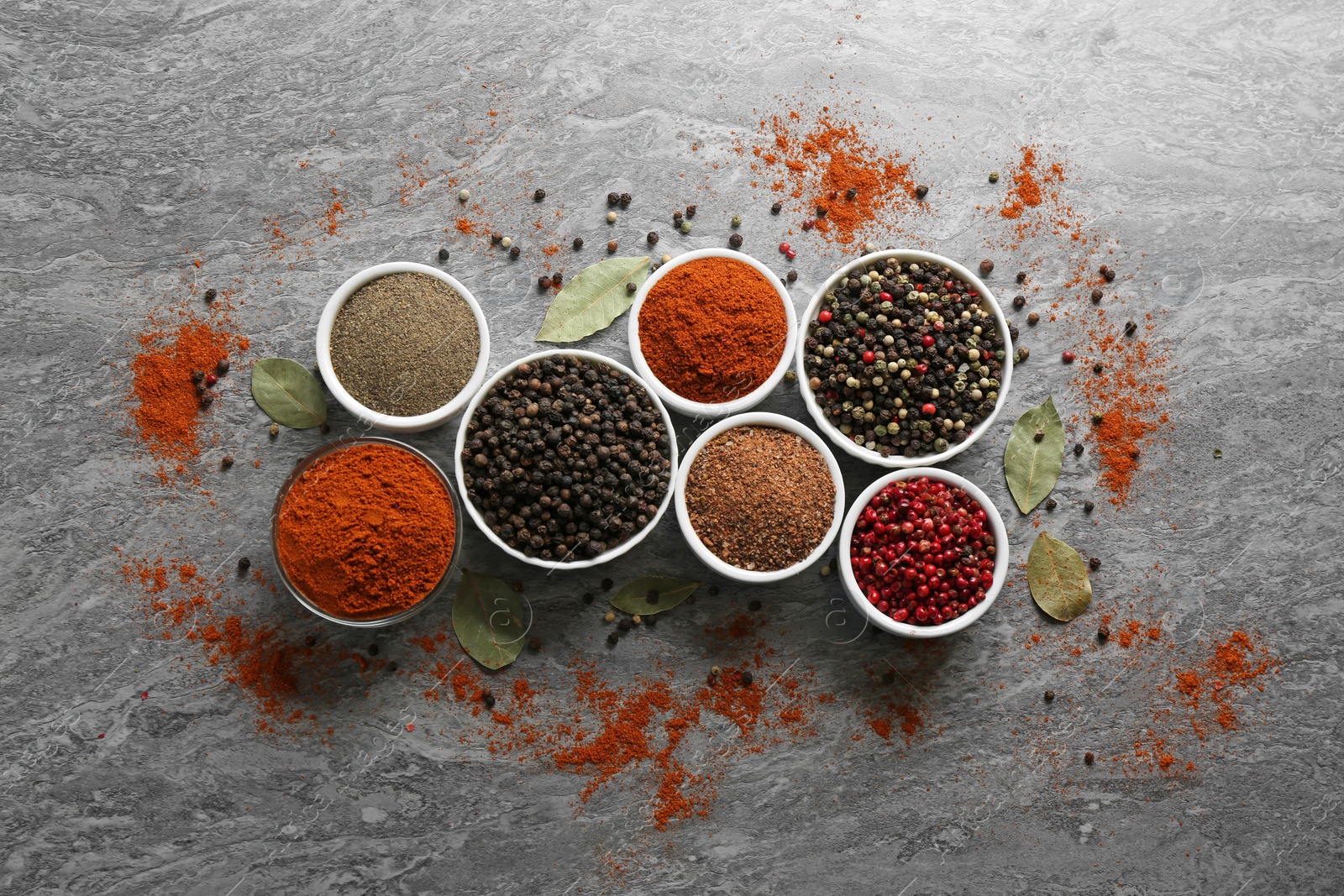Photo of Different ground pepper and corns on grey table, flat lay