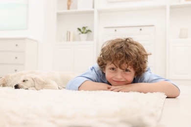Photo of Little boy lying with cute puppies on white carpet at home