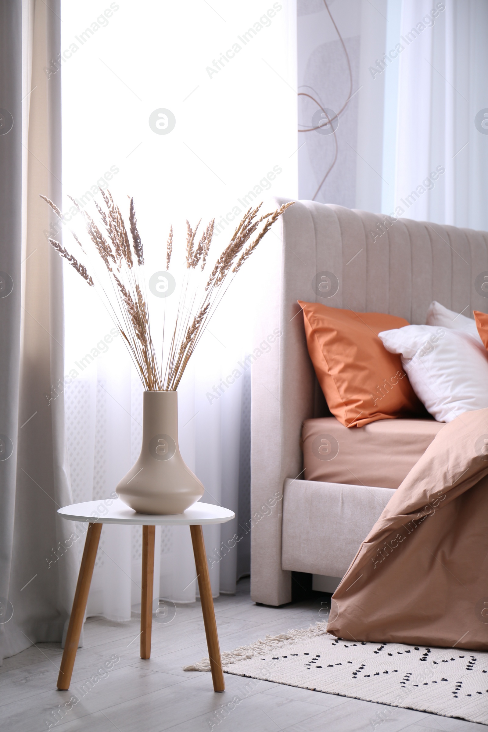 Photo of Vase with decorative dried plants on table in bedroom. Interior design