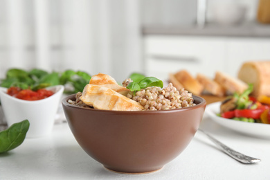 Photo of Tasty buckwheat porridge with meat on white table indoors