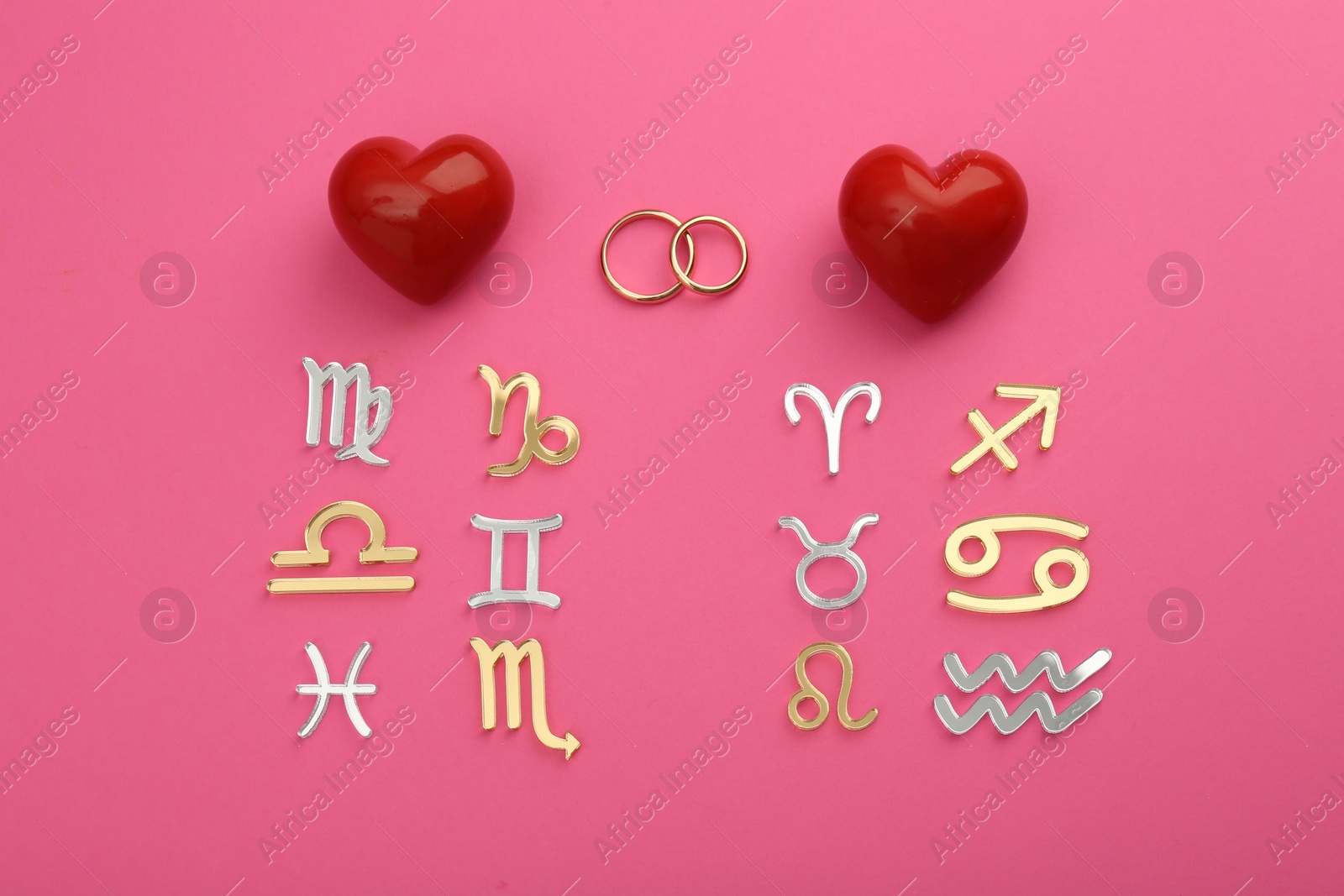 Photo of Zodiac compatibility. Signs, wedding rings and red hearts on pink background, flat lay