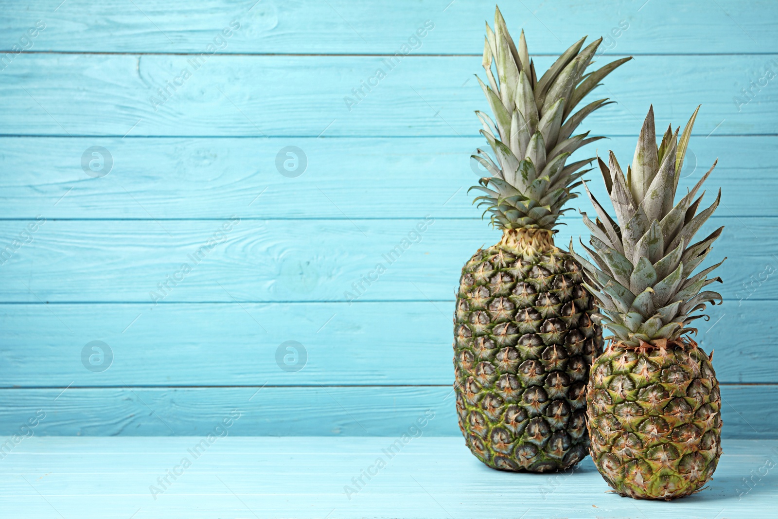 Photo of Fresh delicious pineapples on table against wooden background, space for text