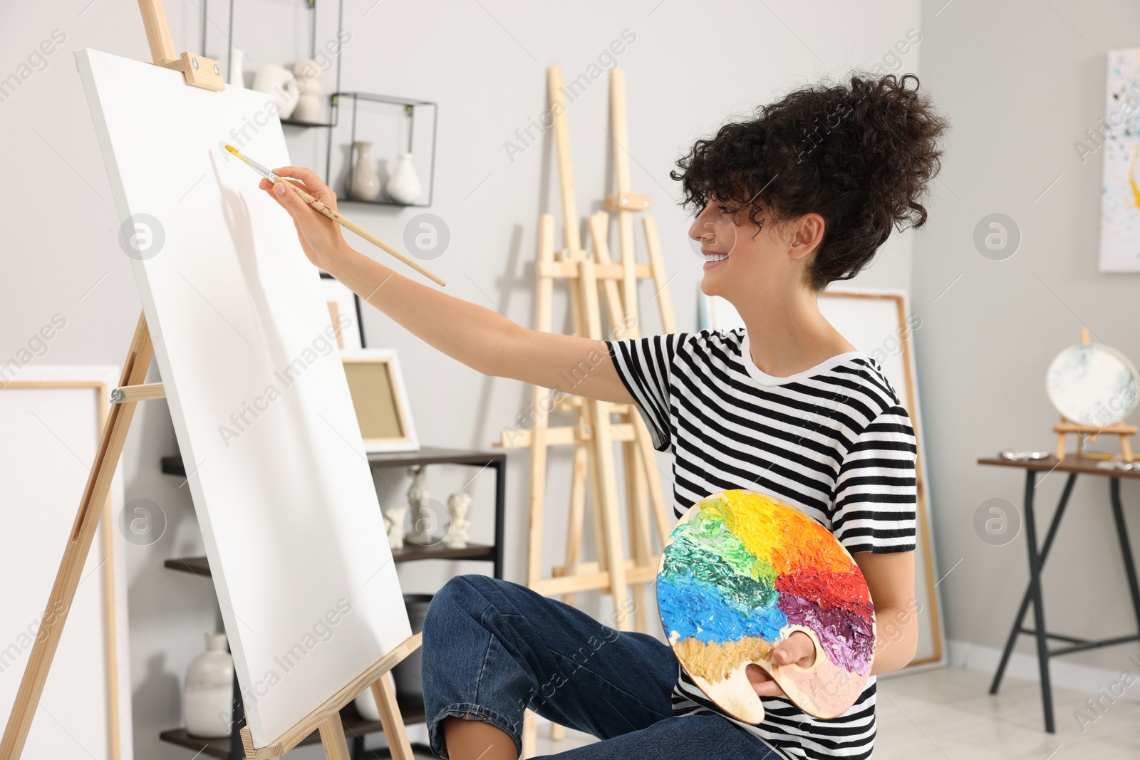 Photo of Young woman painting on easel with canvas in studio