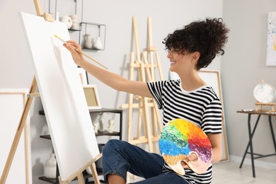 Photo of Young woman painting on easel with canvas in studio