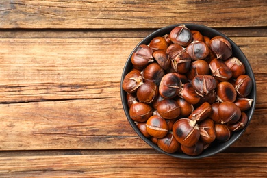 Photo of Delicious roasted edible chestnuts in bowl on wooden table, top view. Space for text