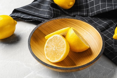 Photo of Bowl with lemons and fabric on light background