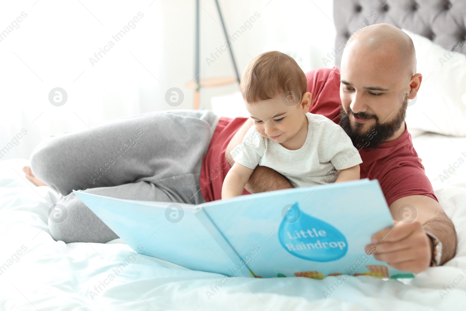 Photo of Dad reading book with his little son in bedroom