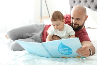 Dad reading book with his little son in bedroom
