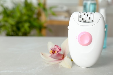 Photo of Modern epilator and beautiful flower on table