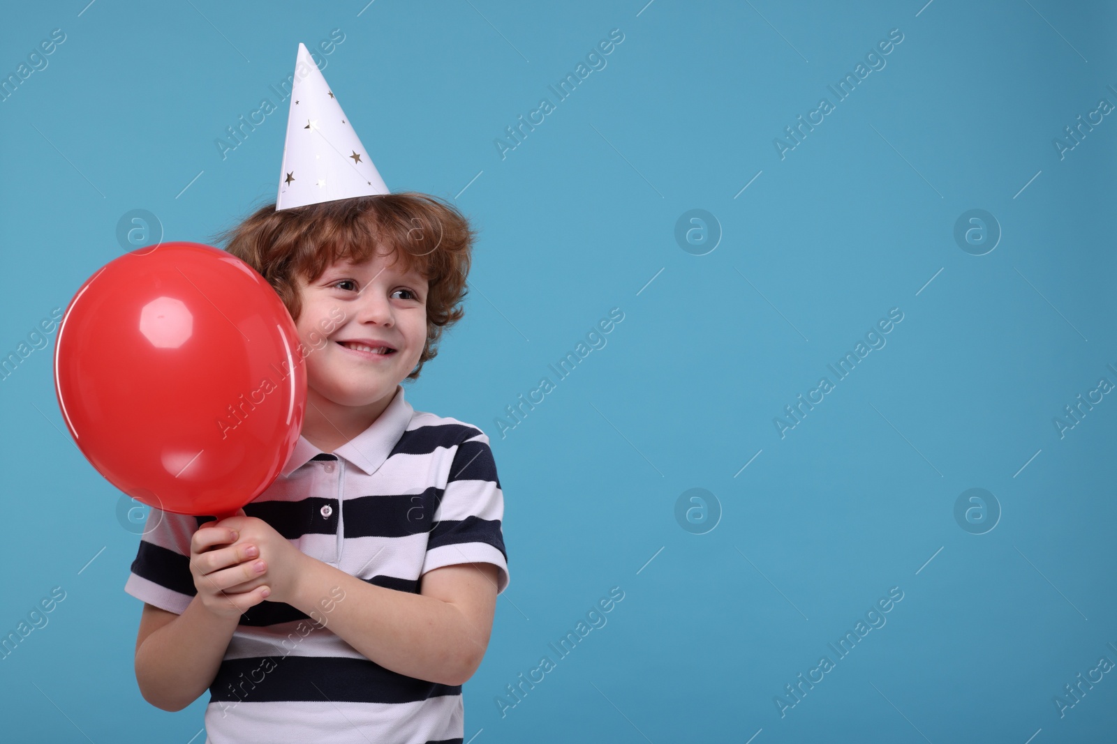 Photo of Happy little boy in party hat with balloon on light blue background. Space for text