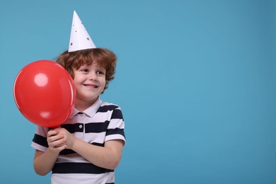 Photo of Happy little boy in party hat with balloon on light blue background. Space for text