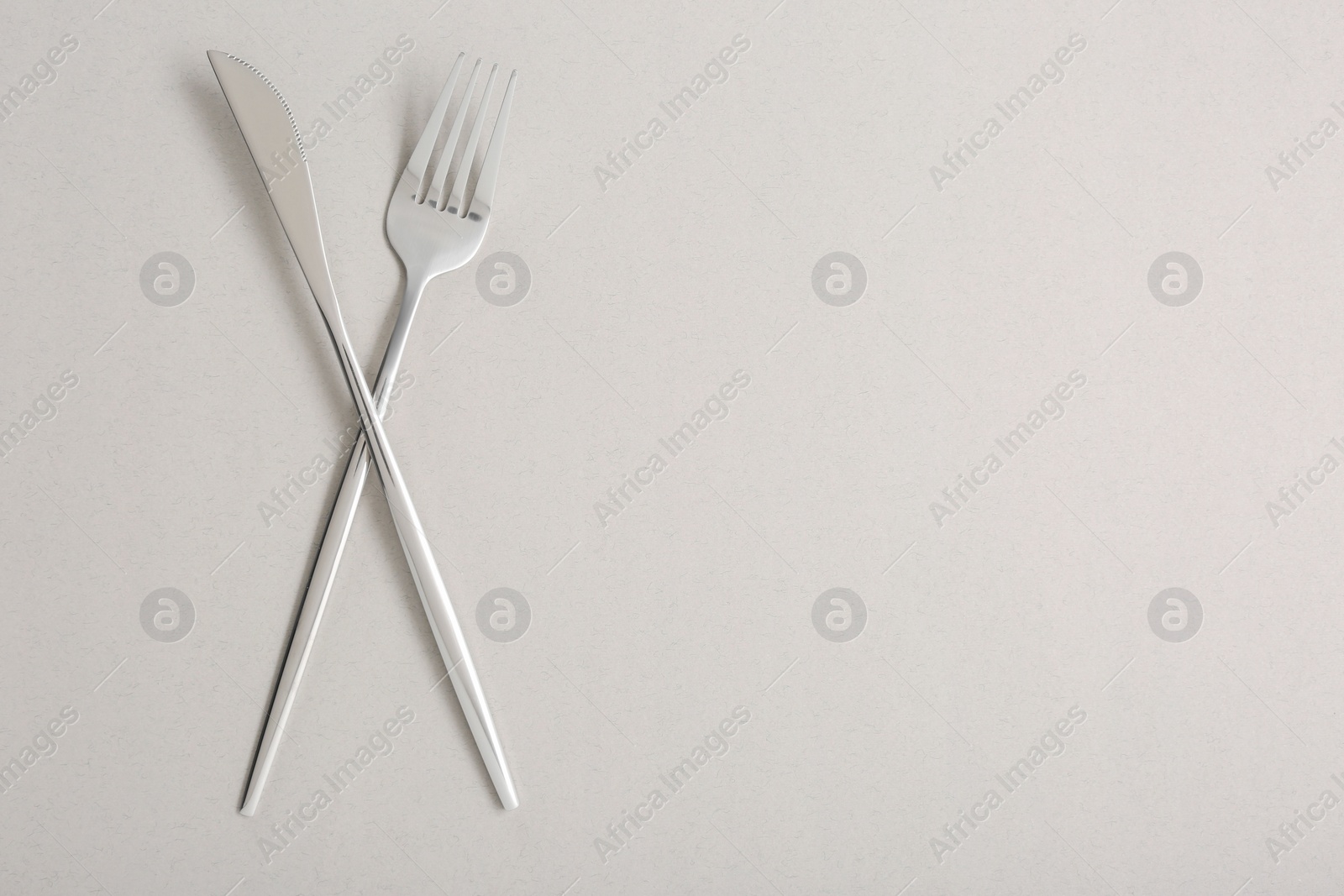 Photo of Shiny fork and knife on light grey background, flat lay. Space for text