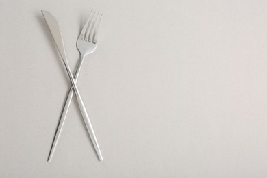 Photo of Shiny fork and knife on light grey background, flat lay. Space for text
