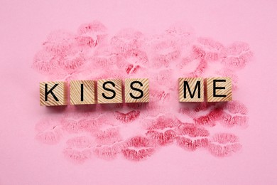 Photo of Wooden cubes with phrase Kiss Me and lipstick marks on pink background, flat lay