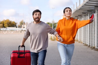 Photo of Being late. Couple with red suitcase running outdoors