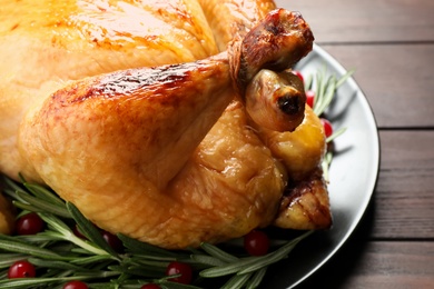 Photo of Delicious cooked turkey served with rosemary and cranberries on wooden table, closeup. Thanksgiving Day celebration