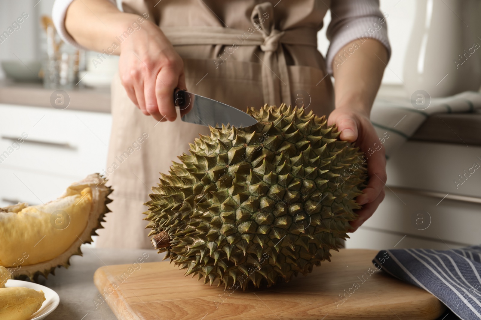 Photo of Woman cutting durian at table in kitchen, closeup