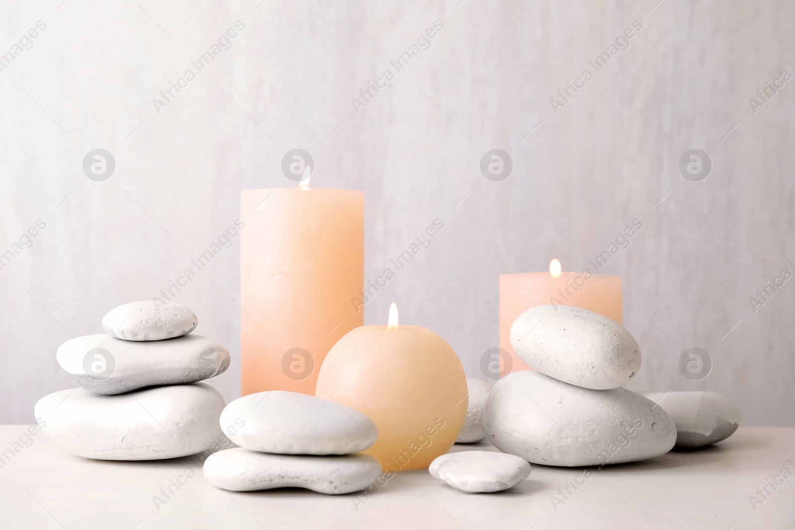 Photo of Zen stones and lighted candles on table against light background