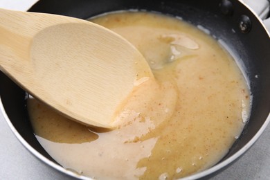 Photo of Stirring delicious turkey gravy in frying pan on table, closeup