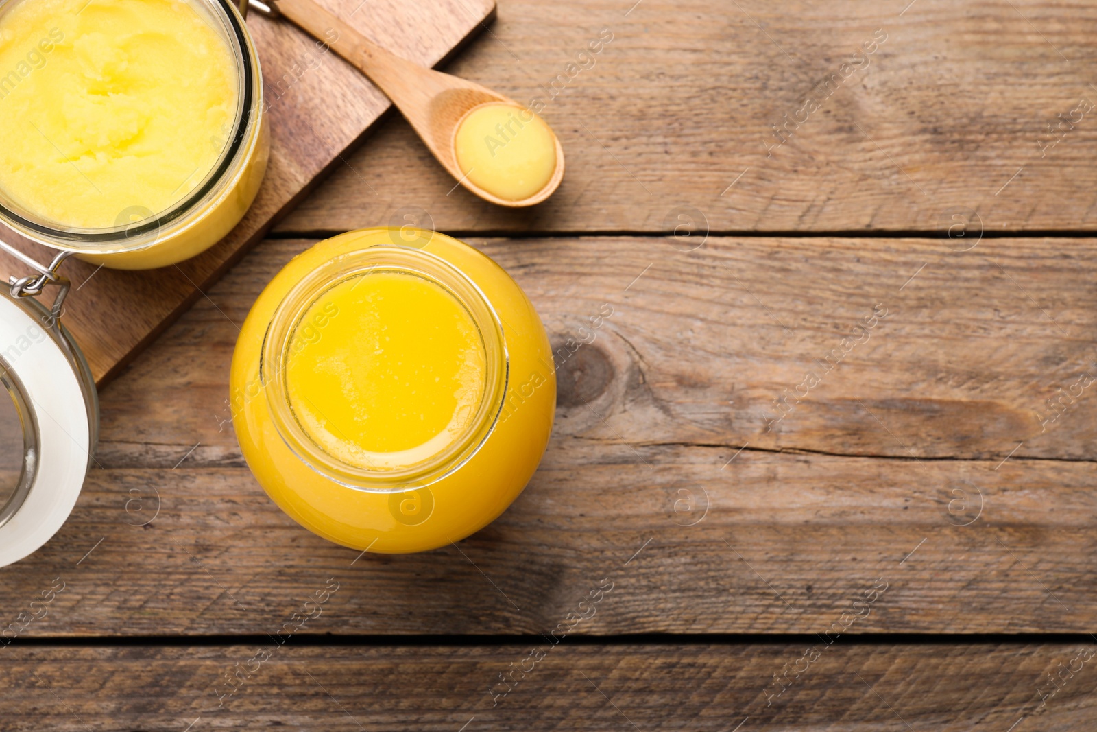 Photo of Glass jars and spoon of Ghee butter on wooden table, flat lay. Space for text