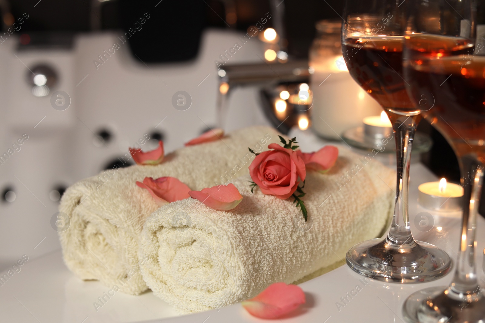 Photo of Glasses of wine, towels and rose on tub in bathroom, closeup. Romantic atmosphere