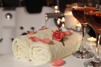 Photo of Glasses of wine, towels and rose on tub in bathroom, closeup. Romantic atmosphere