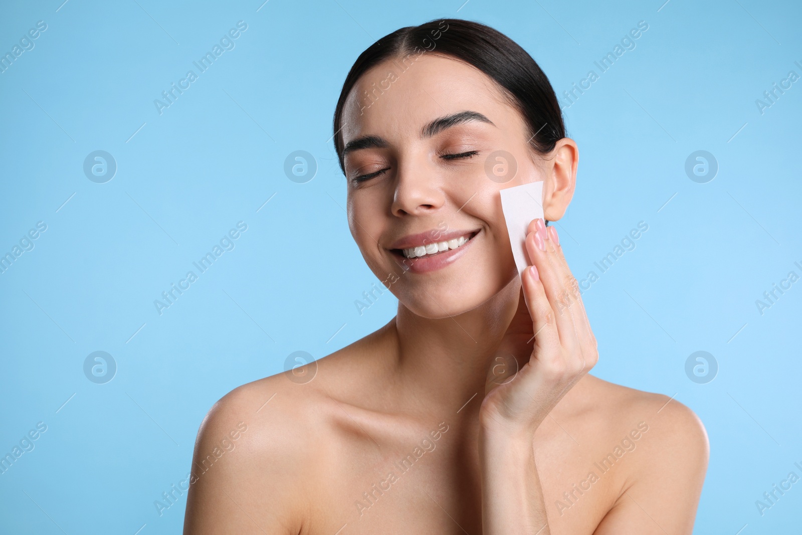 Photo of Beautiful woman using mattifying wipe on light blue background