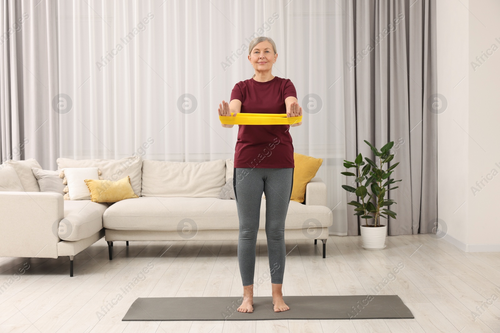 Photo of Senior woman doing exercise with fitness elastic band at home