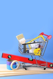 Small shopping cart with paint and renovation equipment on light blue background