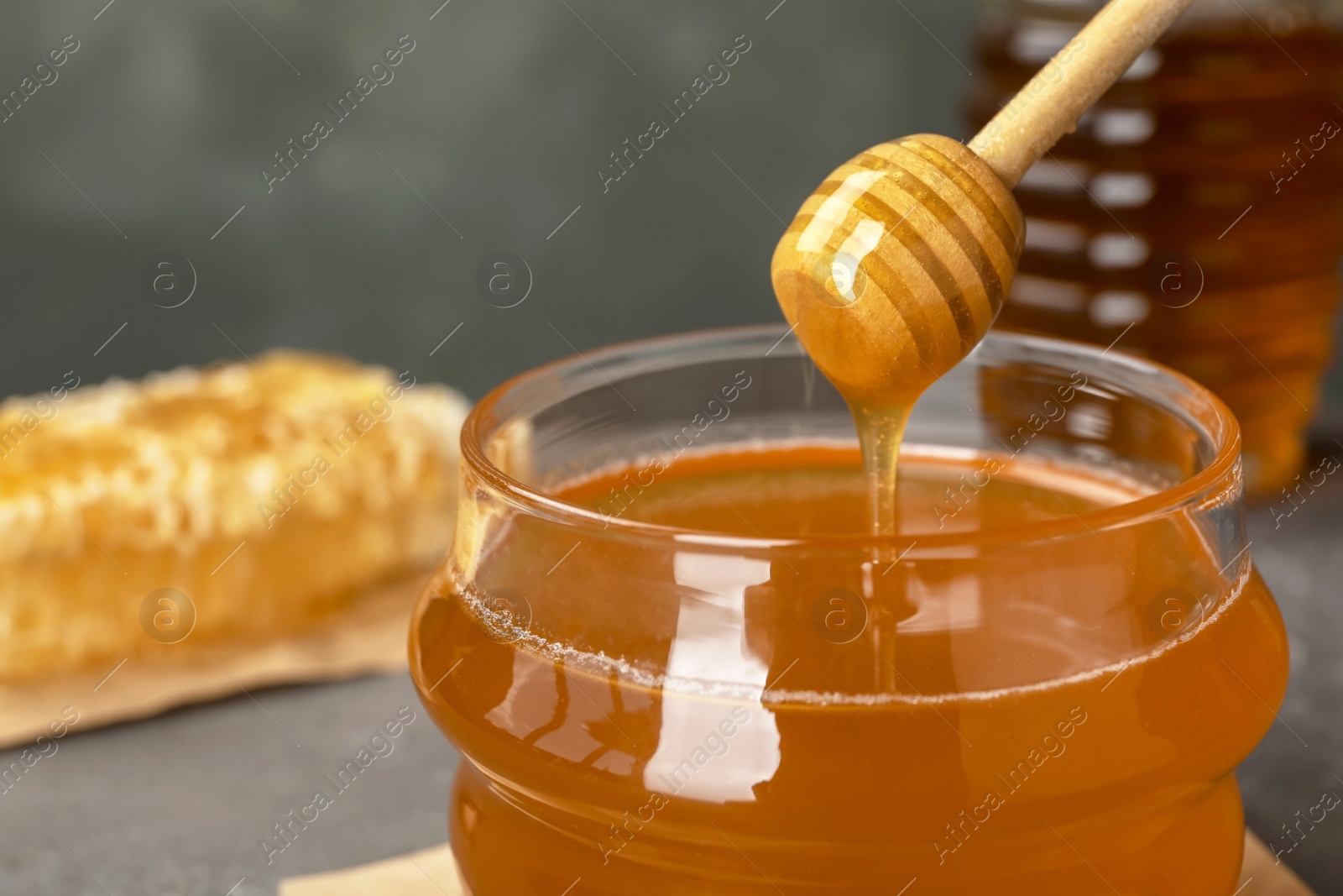 Photo of Sweet honey dripping from dipper into glass jar, closeup