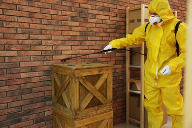 Photo of Pest control worker spraying pesticide on wooden crate indoors