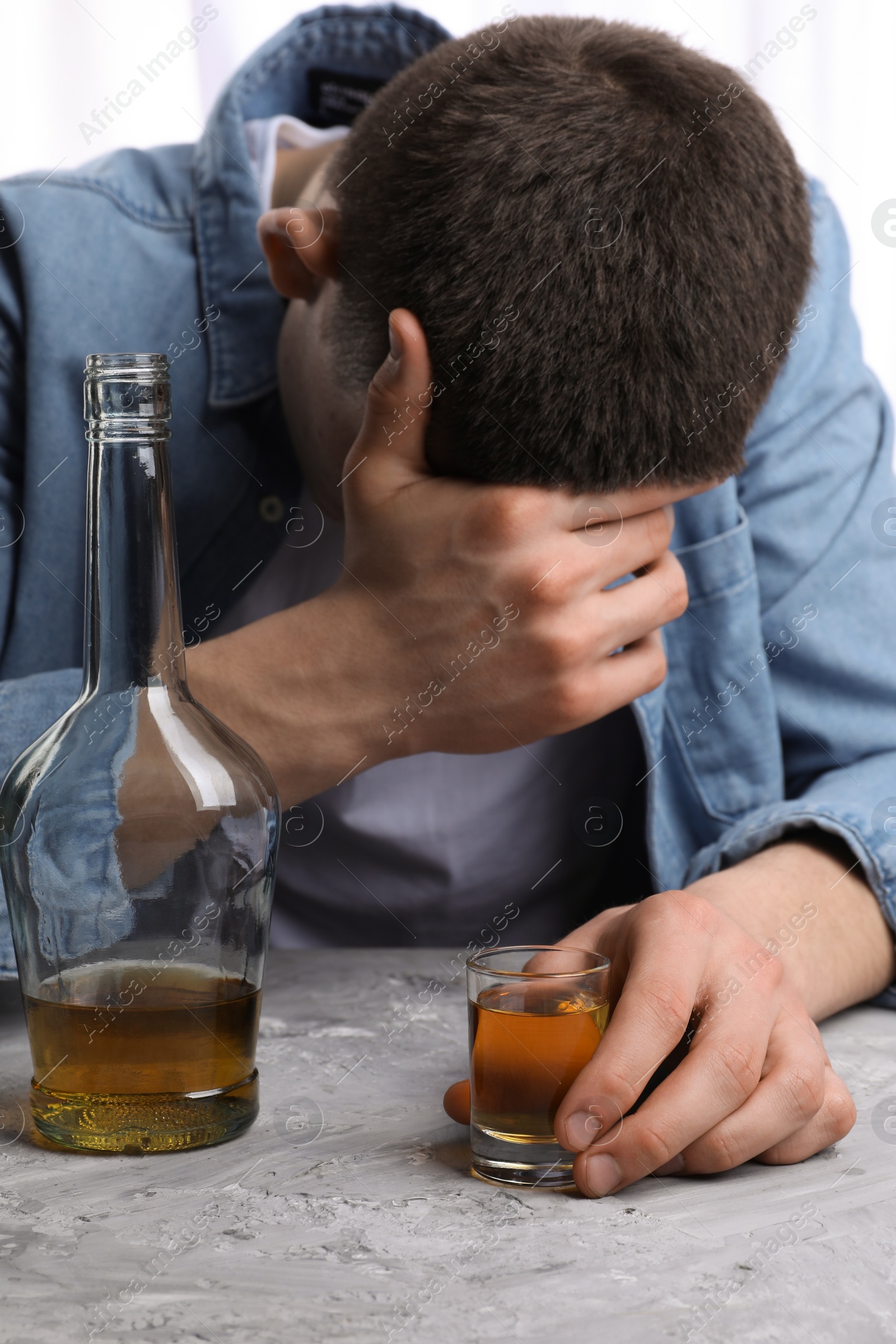 Photo of Alcohol addiction. Man with whiskey at grey textured table