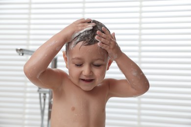Photo of Cute little boy washing hair with shampoo in bathroom