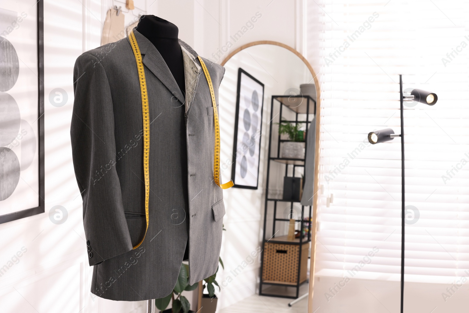 Photo of Mannequin with unfinished jacket and measuring tape in tailor shop, space for text