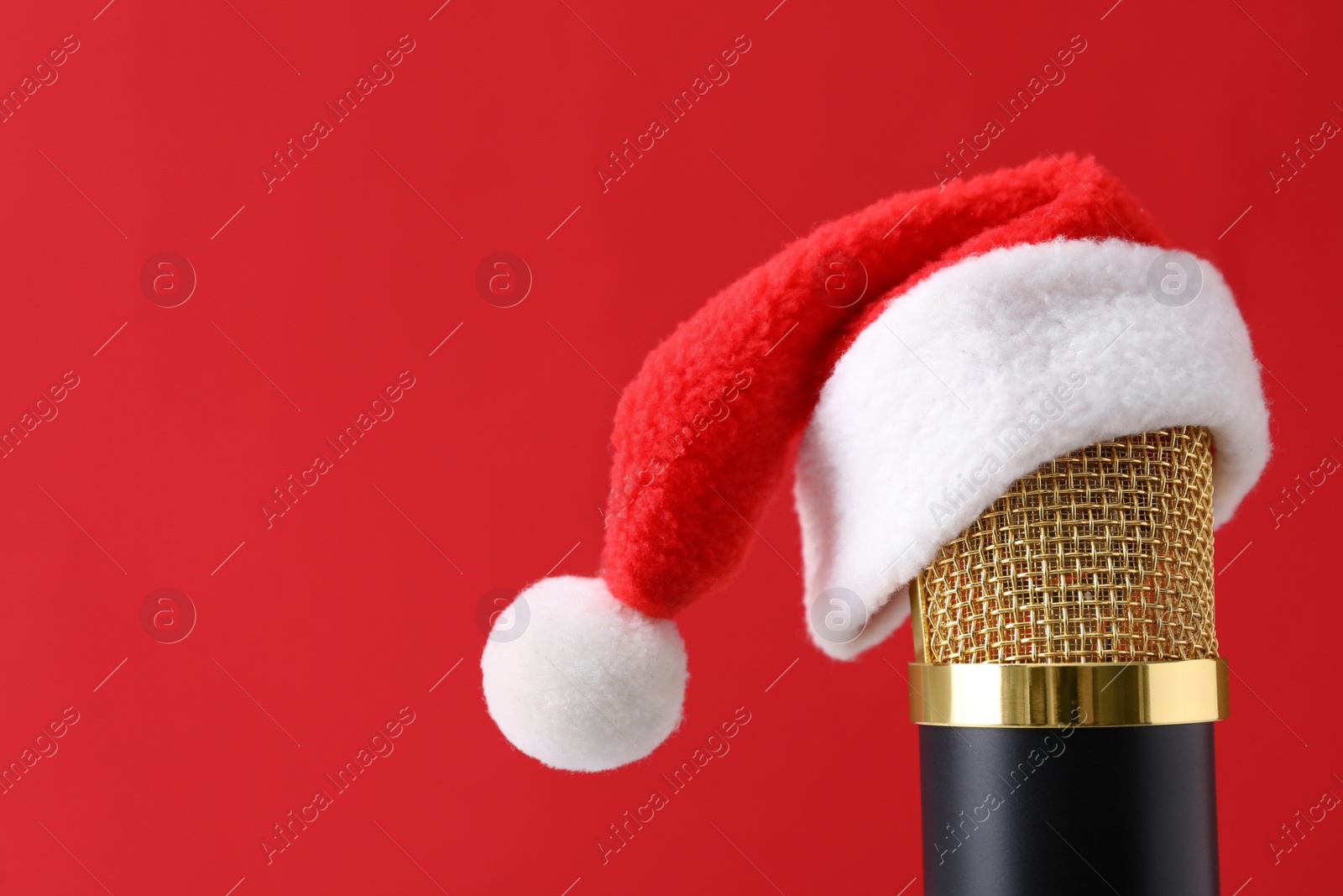 Photo of Microphone with Santa hat on red background, space for text. Christmas music