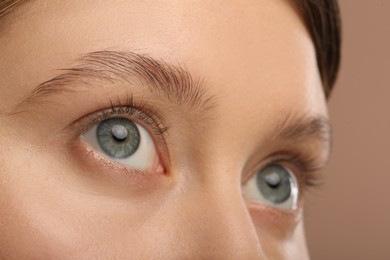 Woman with beautiful natural eyelashes on light brown background, closeup