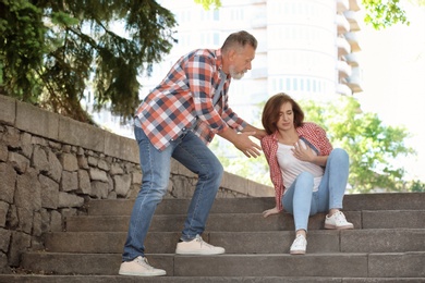 Man helping mature woman suffering from heart attack on stairs, outdoors