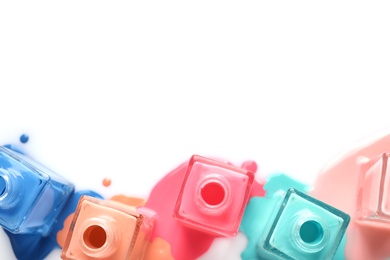 Photo of Spilled different nail polishes with bottles on white background, top view