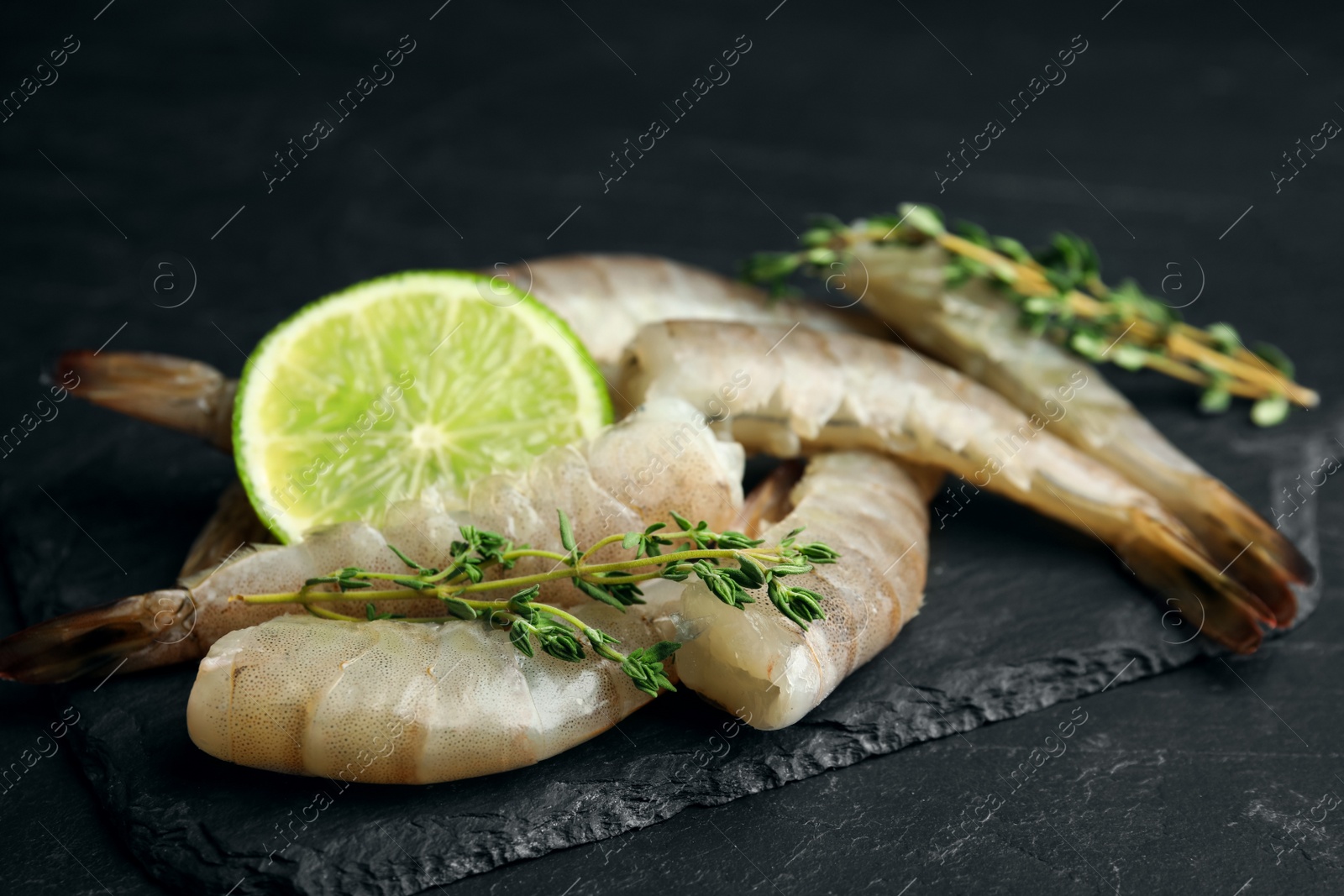 Photo of Fresh raw shrimps with lime and thyme on black table, closeup