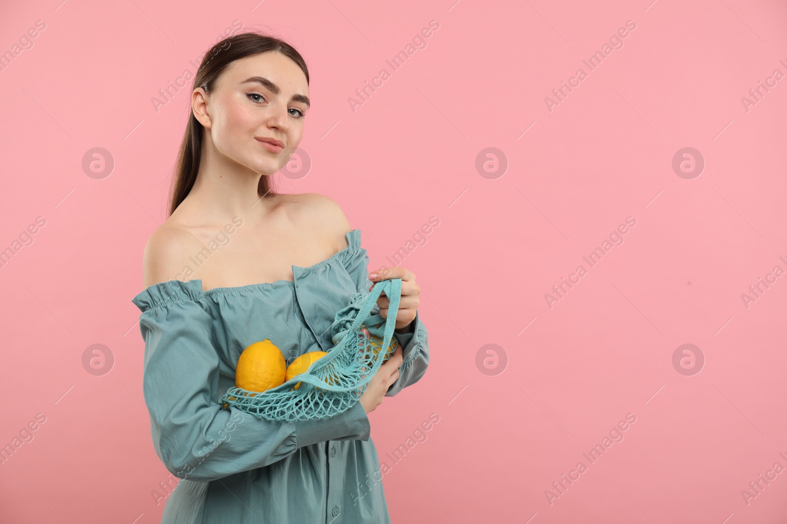 Photo of Woman with string bag of fresh lemons on pink background, space for text