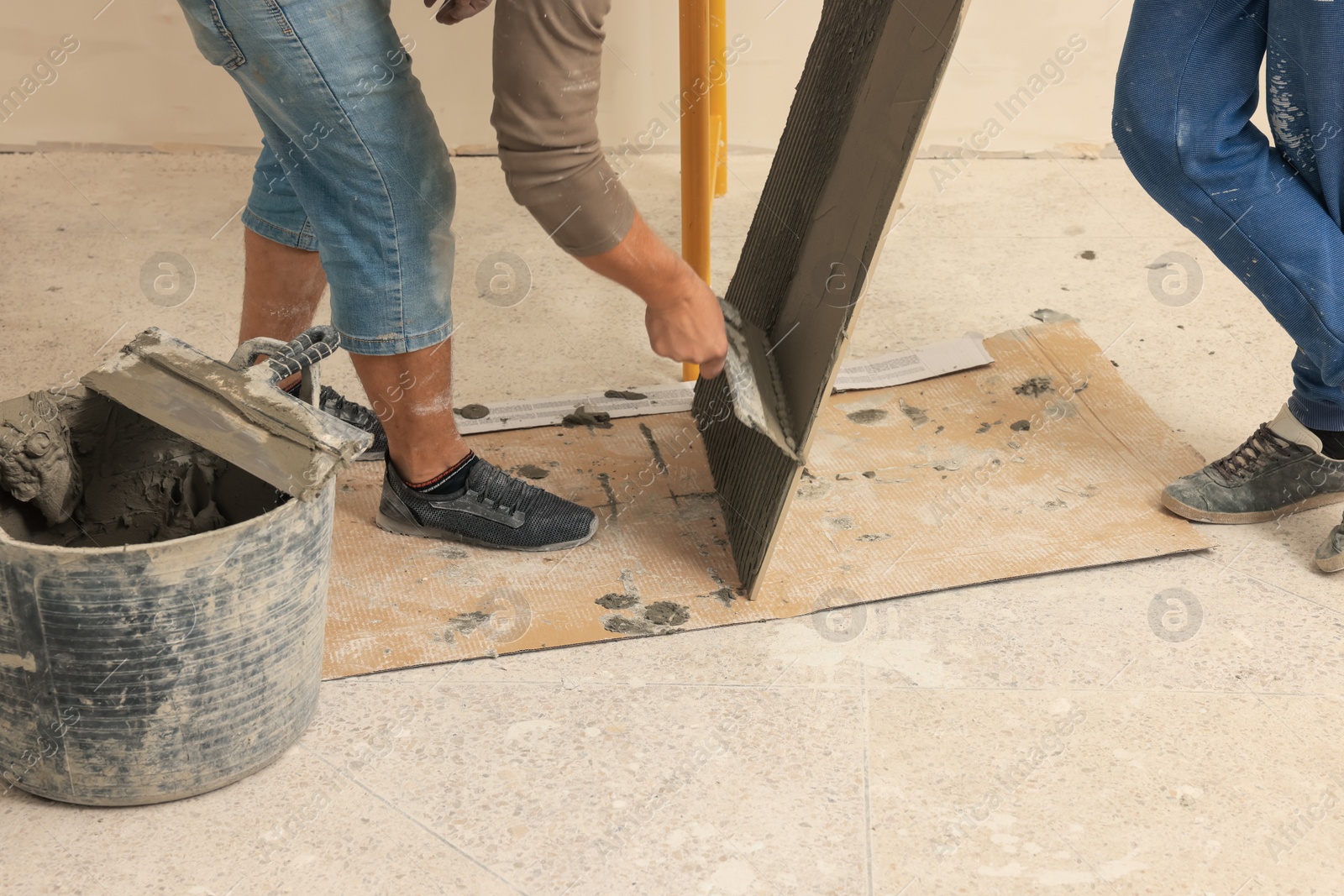 Photo of Worker spreading adhesive mix over tile with spatula, closeup