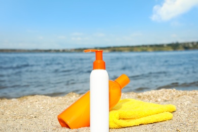 Bottles of sun protection body cream and towel on beach, space for design