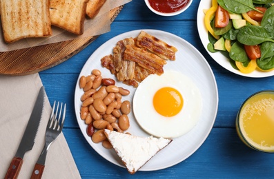 Tasty breakfast with fried egg, beans and bacon served on blue wooden table, flat lay