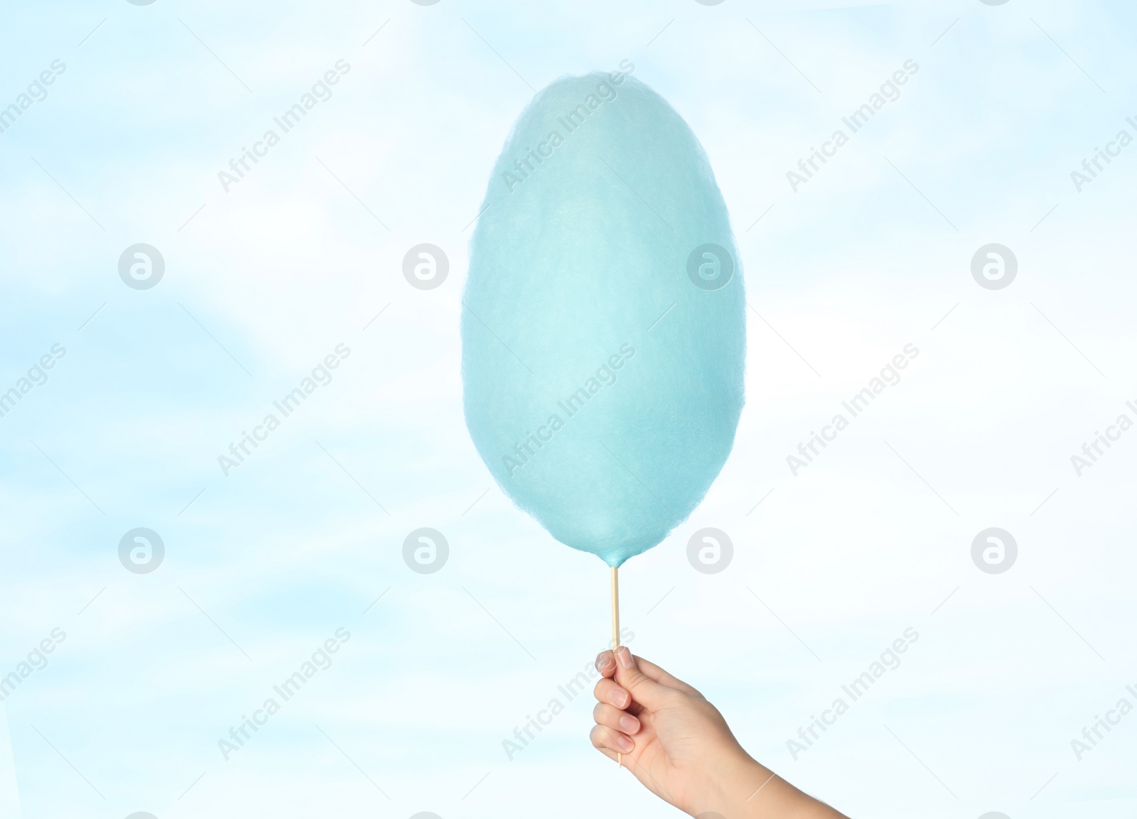Photo of Woman holding sweet cotton candy on blue sky background, closeup view