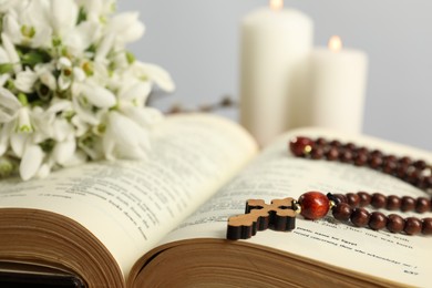 Photo of Bible, rosary beads, flowers and church candles on table, closeup