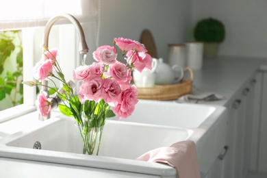 Photo of Pouring water into glass vase with flowers near window in kitchen, space for text