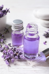 Photo of Glass bottles of natural cosmetic oil and lavender flowers on white wooden table